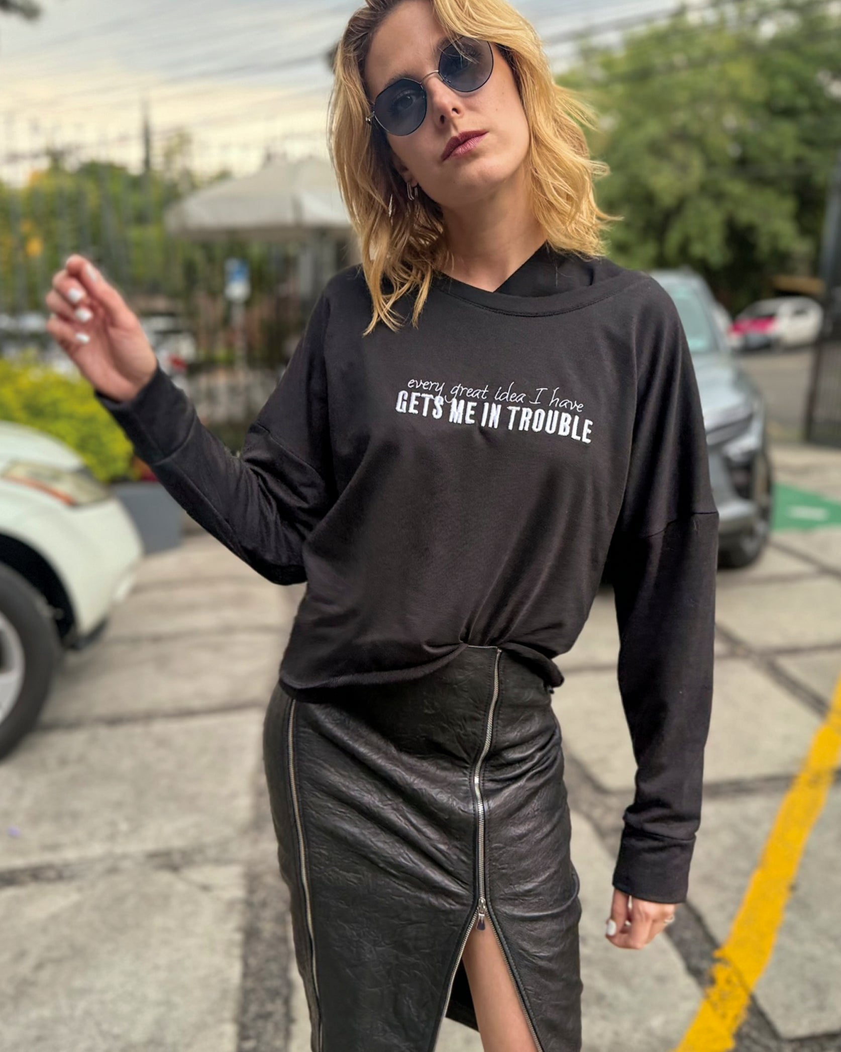 Modelo usando Sweat Crop oversized negra de In-Diferente Fashion con el mensaje 'Every Great Idea I Have Gets Me In Trouble' y falda de cuero negra.
