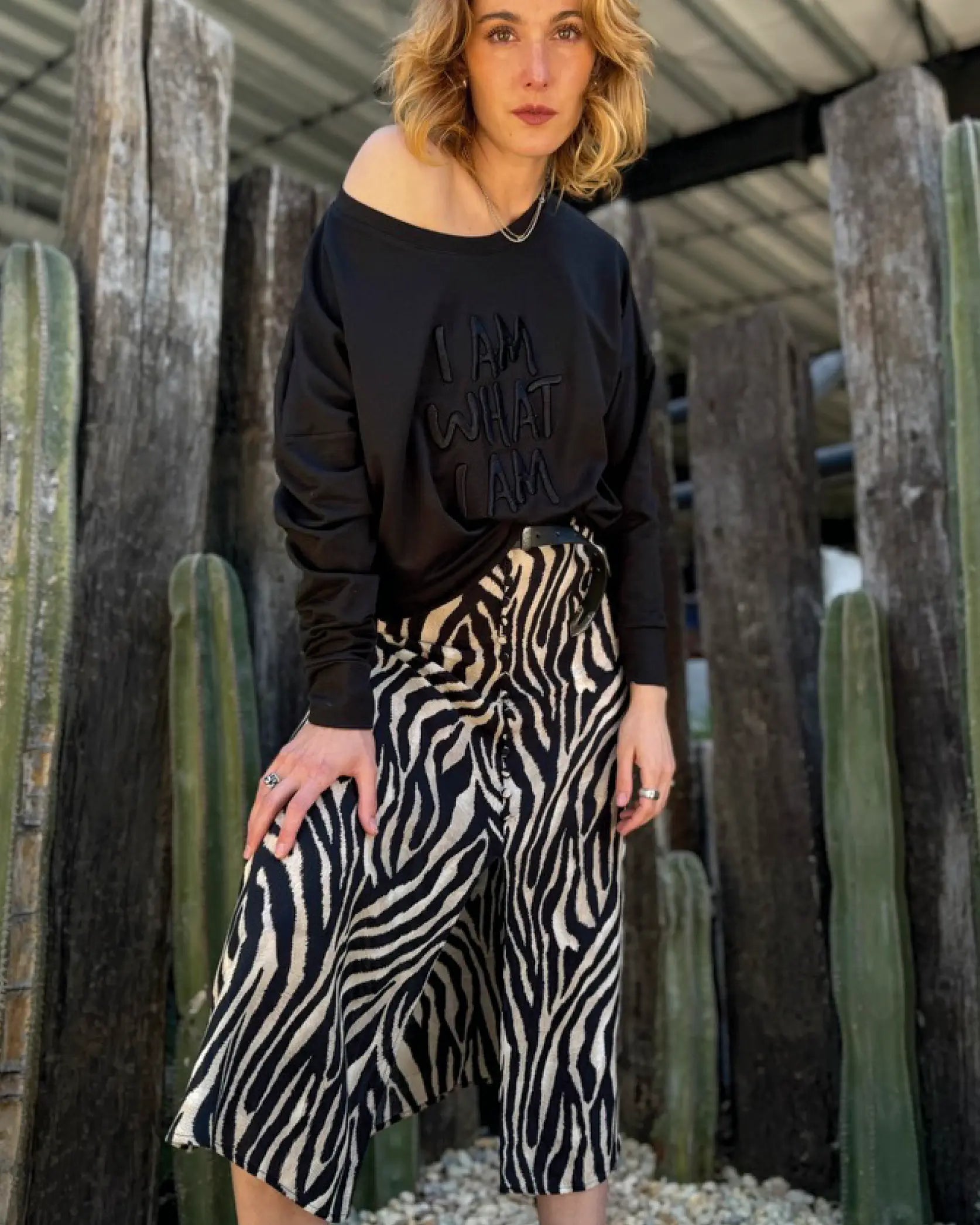 Modelo usando Sweat Crop oversized negra de In-Diferente Fashion con el mensaje 'I Am What I Am' bordado en el frente, mostrando la caída fluida del french terry de algodón Pima