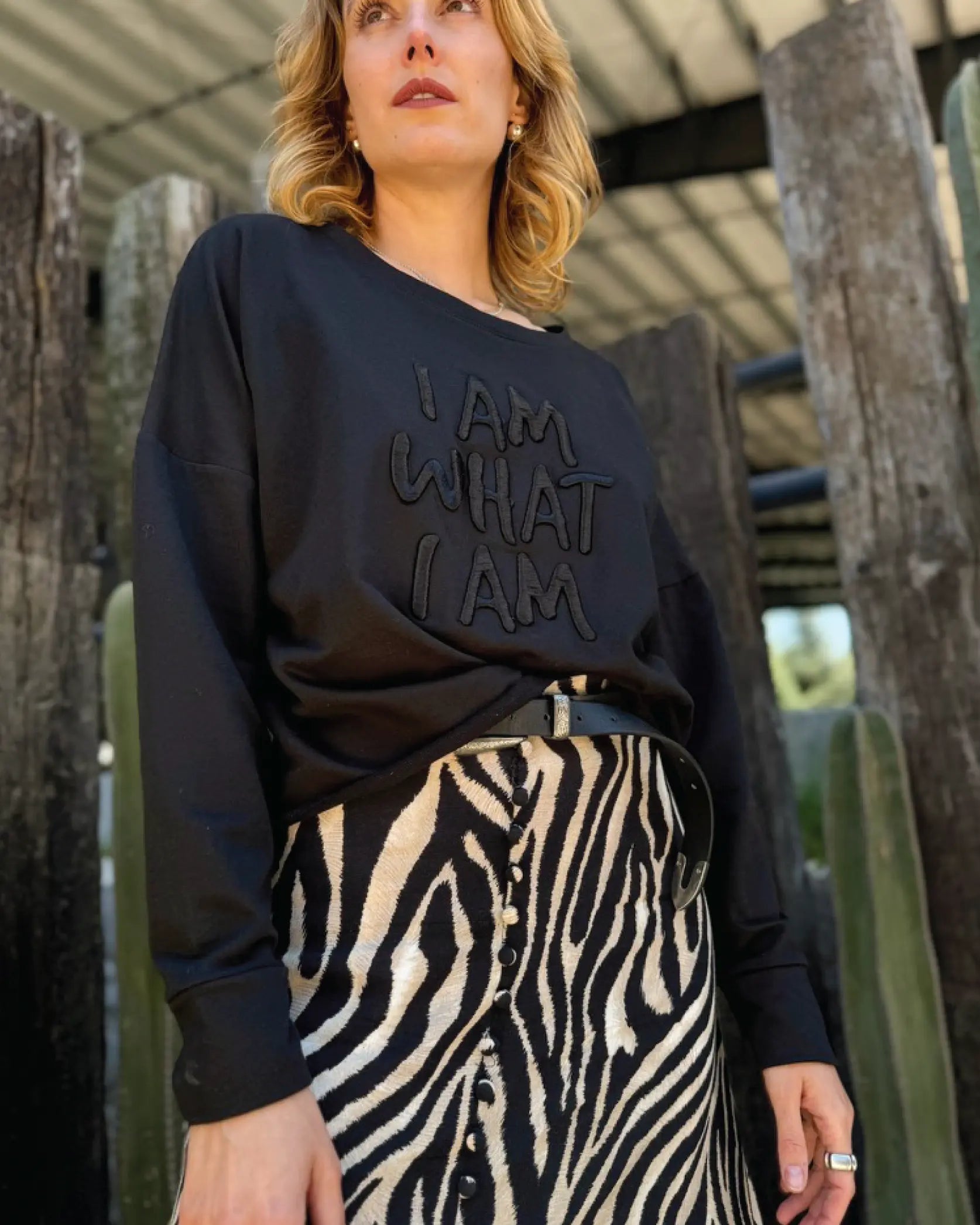 Modelo usando Sweat Crop oversized negra de In-Diferente Fashion con el mensaje 'I Am What I Am' bordado en alto relieve monocromático