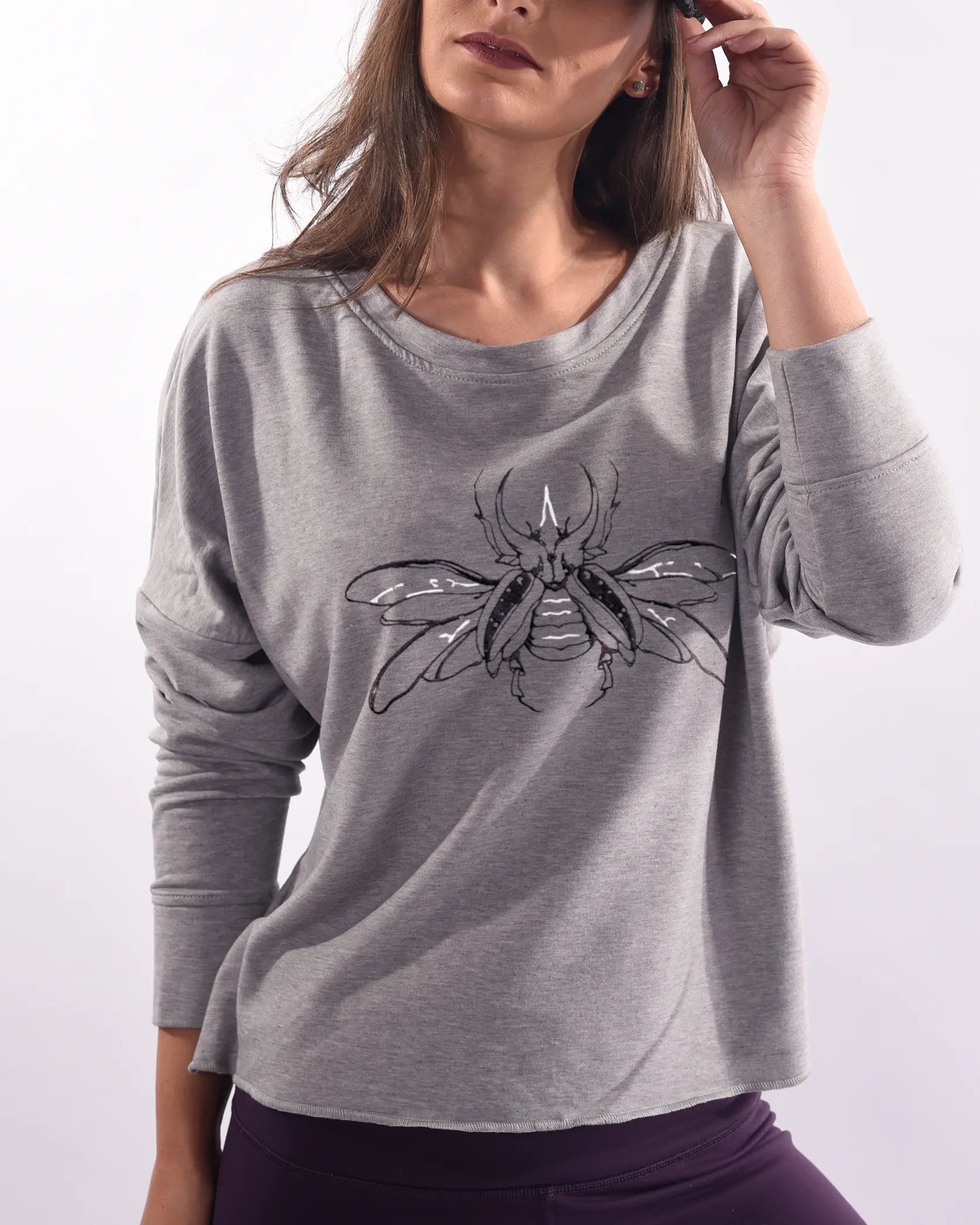 Modelo usando Sweat Crop oversized gris de In-Diferente Fashion con bordado de escarabajo en negro y blanco en el frente, mostrando la caída del french terry de algodón Pima