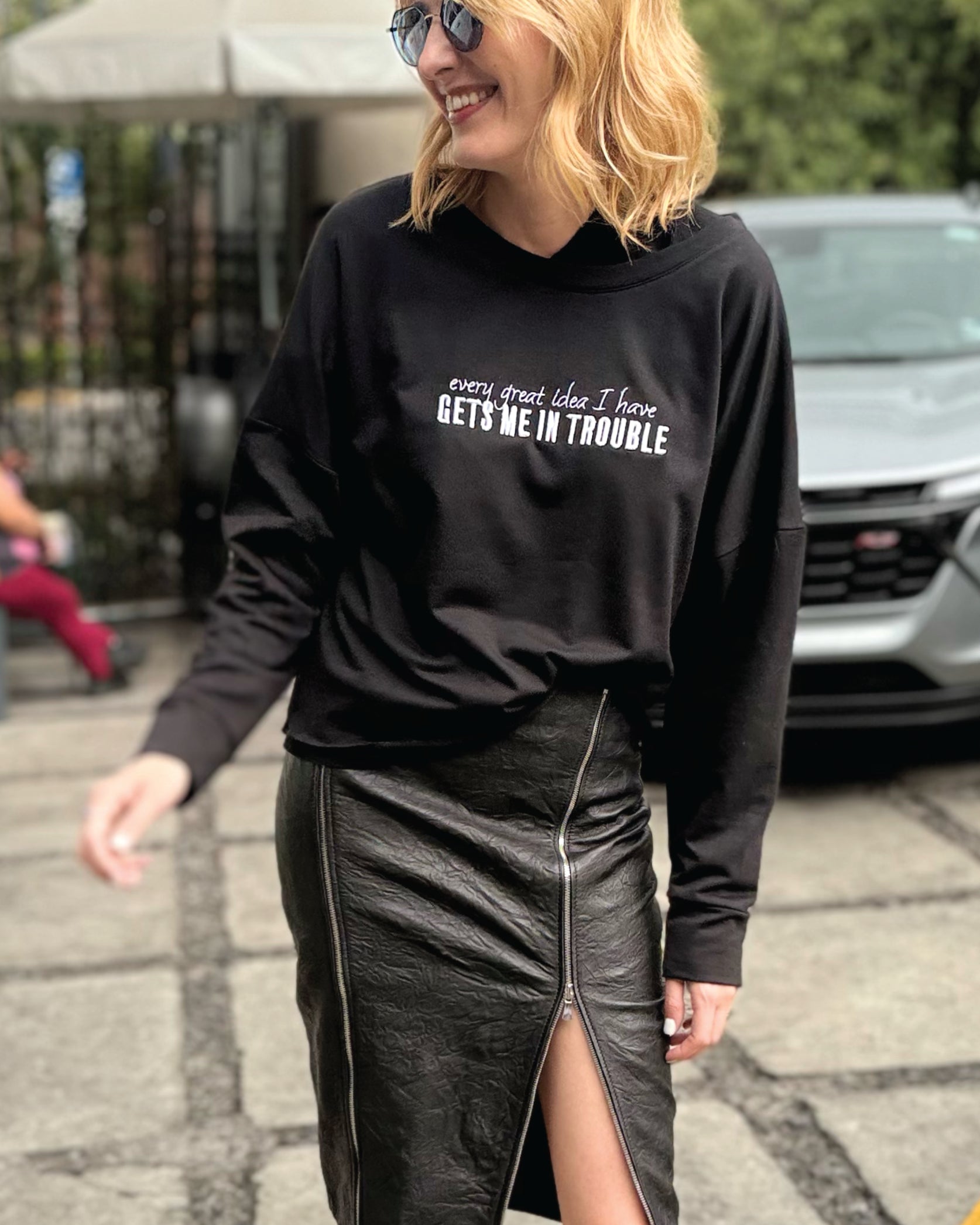 Modelo usando Sweat Crop oversized negra de In-Diferente Fashion con el mensaje 'Every Great Idea I Have Gets Me In Trouble' bordado en blanco brillante en el frente, mostrando la caída fluida del french terry de algodón Pima.