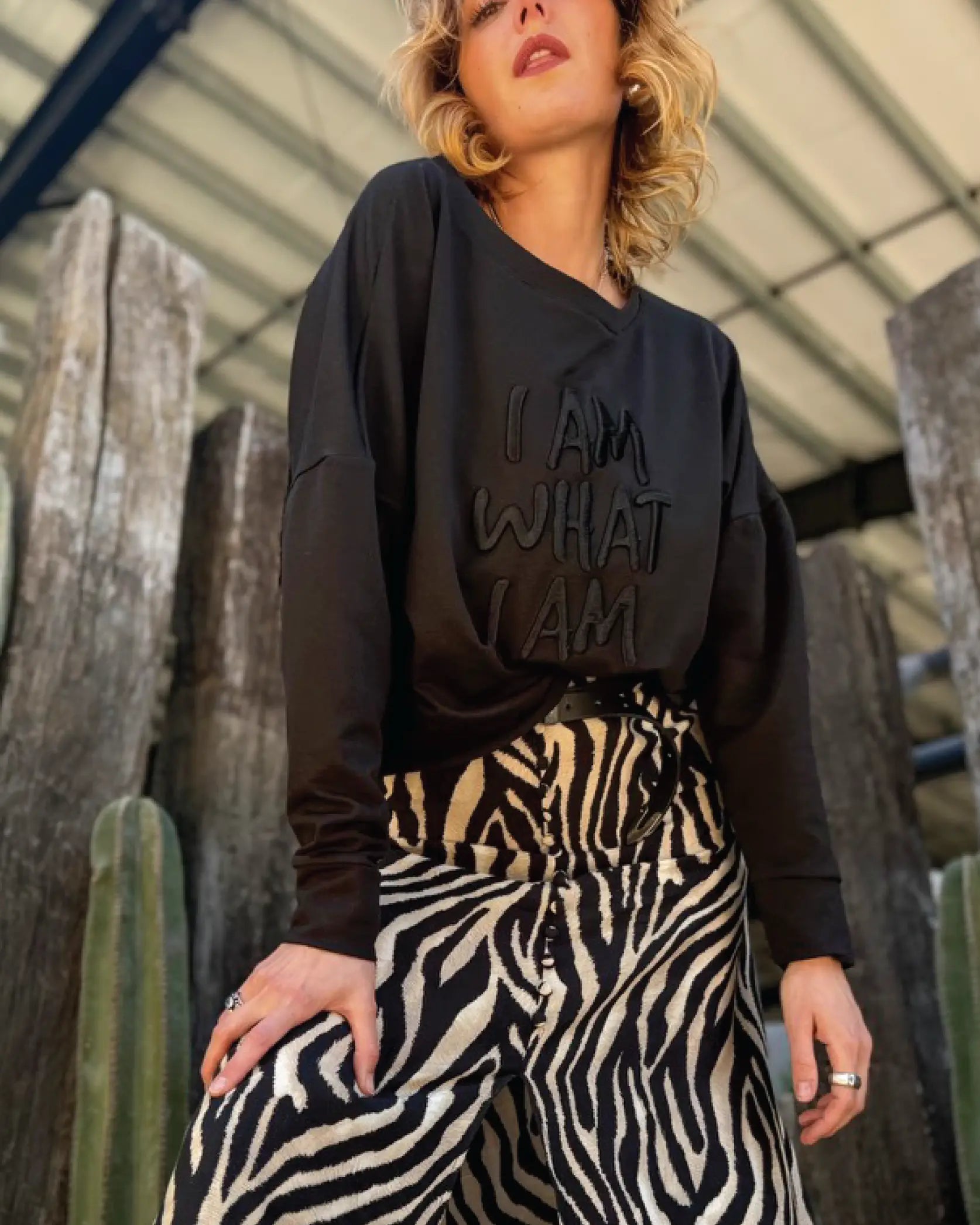 Modelo usando Sweat Crop oversized negra de In-Diferente Fashion con el mensaje 'I Am What I Am' bordado en alto relieve tonal en el frente, mostrando la caída fluida del french terry de algodón Pima