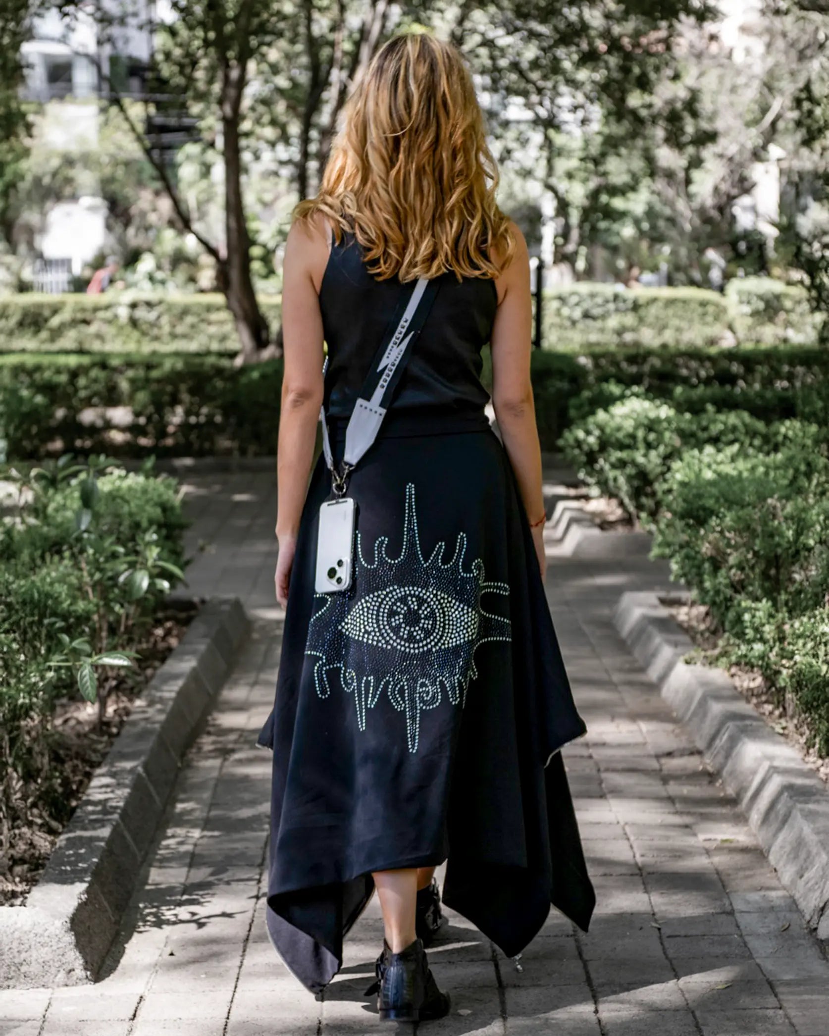 Modelo usando Capa Falda transformable negra 'Ojo de Cristales' de In-Diferente Fashion, con cristales brillantes en la espalda, mostrando su uso como falda vista trasera